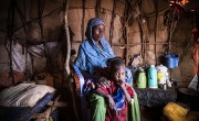Child standing between legs of concerned mother in hut