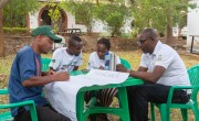 Four people at green plastic table writing list on large sheet of paper