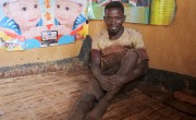 Egide Niyonkurum, a casual labourer, sitting on ground in front of posters