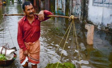 An Indian vegetable vendor carries his wares through floodwaters in Siliguri, West Bengal, on July 24, 2016. AFP/Diptendu Dutta 2016.