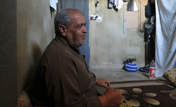 Ibrahim seated in his home, recounting the stresses of being a refugee.