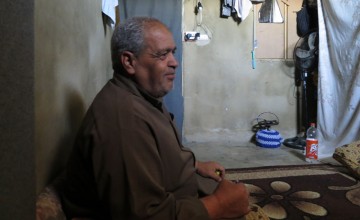 Ibrahim seated in his home, recounting the stresses of being a refugee.