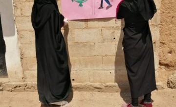 Two women in scarves pasting poster to wall