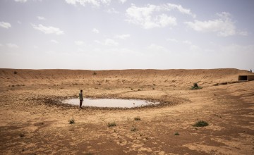 Man standing by nearly dry dam in middle of desert