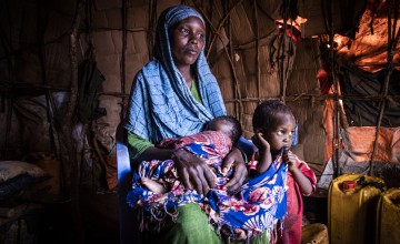 Woman looking off into the distance in makeshift tent holding two young children
