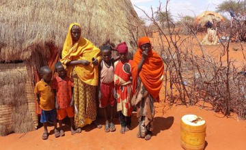Woman in yellow headscarf with five children outside hut