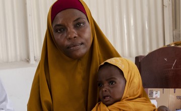 Woman in yellow hijab holding crying baby in matching hijab
