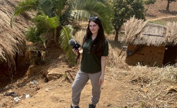 Woman with long brown hair standing in front of huts and trees