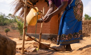 Woman in long skirt stepping on wood to activate jerry can tap 