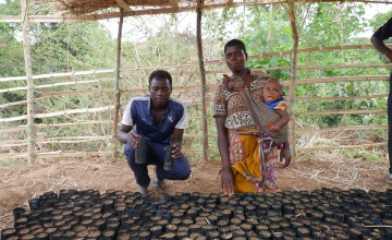 Man and woman with baby in sling around her body show off plastic tubes containing seedlings