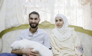 Bearded man smiling and holding baby next to woman in headscarf
