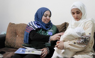 Woman in blue headscarf smiling at baby held by woman in white headscarf