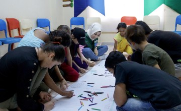 Children and Concern staff sitting on ground and drawing on long strip of white paper