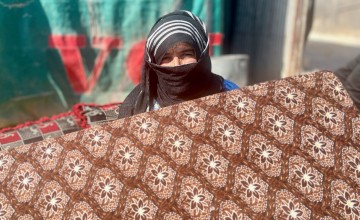 A woman holds a mattress outside of her tent