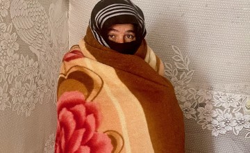 A woman stands in a tent wrapped in a thick fleece blanket