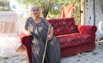 Meryem Kaya holds a cane and sits on couch at remains of her home