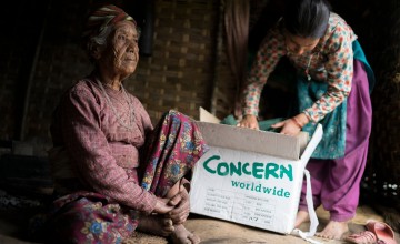 Ratna Khatri, 88 years of age and a previous survivor of the devastating 1934 earthquake, sits in the makeshift shelter her family have built since their home was destroyed in the earthquake as her granddaughter goes through the box of supplies that Concern distributed. Photo: Brian Sokol/Panos Pictures/Concern Worldwide
