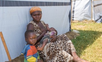 Solange leans against her temporary shelter with her two young daughters Precia and Jessica. Photo taken by Irénée Nduwayezu/Concern Worldwide.