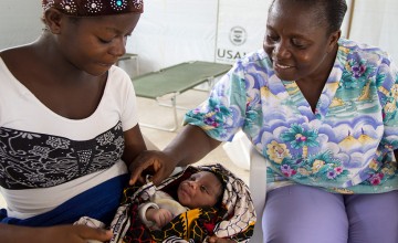 Eighteen year old Doris Kpah cradles her newborn baby under the proud gaze of Alice M Narmah, Nurse Midwife at John Logan Town Community Care Center. Photo taken by Kieran McConville/Concern Worldwide.