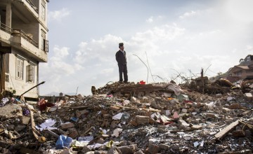 a man standing on the rubble of a building left by the Nepal earthquake. Photo: Helvetas. 