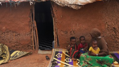 Woman sitting on rug outside clay house with three children