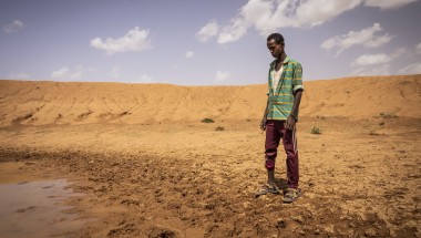 Man in green shirt looking disappointed at nearly dry dam