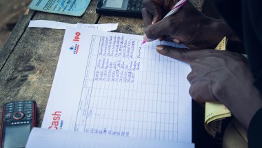 Hands writing details in a cash transfer notebook