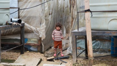 A Syrian refugee child stands next to the water tanks at an informal tented settlement in in Akkar, northern Lebanon. Photo taken by Dalia Khamissy / Concern Worldwide.