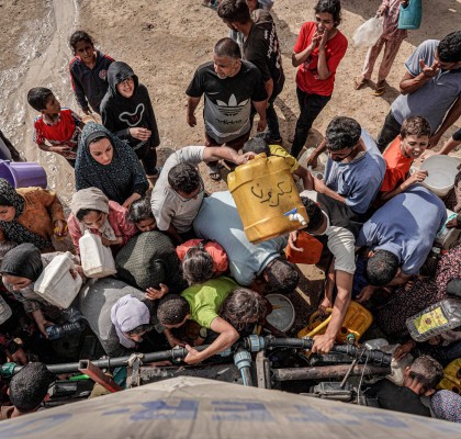 People gather with jerrycans and other containers to collect water from a tanker cistern in Deir el-Balah in the central Gaza Strip