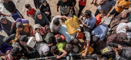 People gather with jerrycans and other containers to collect water from a tanker cistern in Deir el-Balah in the central Gaza Strip