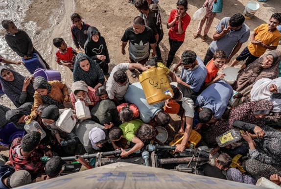 People gather with jerrycans and other containers to collect water from a tanker cistern in Deir el-Balah in the central Gaza Strip