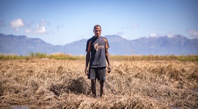 Recently married Patrick Ghembo of Monyo Village standing in his field, destroyed by the floods. Patrick is a farmer of maize and rice. He must rely solely on fishing until he can plant again. His wife and him will stay at the displacement camp until the floods have fully subsided. Photo: Gavin Douglas/ Concern Worldwide.