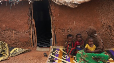 Woman sitting on rug outside clay house with three children