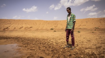 Man in green shirt looking disappointed at nearly dry dam