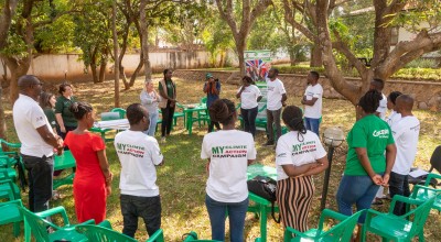 Group of people standing in a circle in a garden in front of green plastic chairs