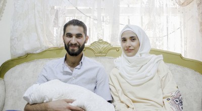 Bearded man smiling and holding baby next to woman in headscarf