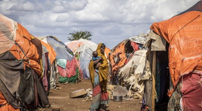 Somalian woman carrying child, surrounded by informal tents 