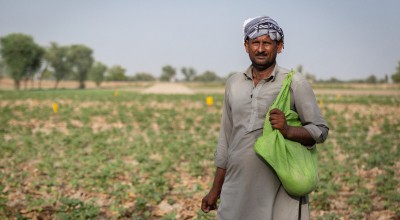 Farmer Maula stands in field in Pakistan with green bag of seeds