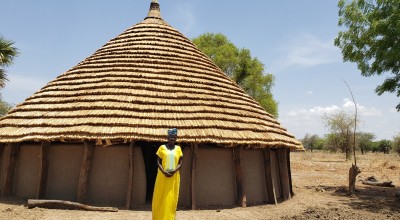 Abuk Wieu in front of her tukul house constructed using savings from the Village Savings and Loans Association.