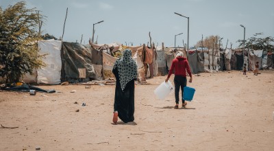 A mother and children returning to her tent within camp after receiving her cholera/hygiene kit, Al-Salam City IDP camp, Dar Saad district, Aden Governorate. (Photo: Ammar Khalaf/Concern Worldwide)