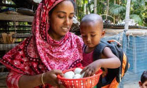 Woman in pink headscarf holding infant son and basket of eggs