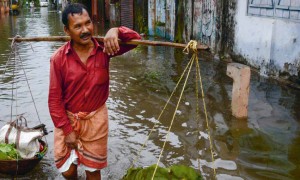 An Indian vegetable vendor carries his wares through floodwaters in Siliguri, West Bengal, on July 24, 2016. AFP/Diptendu Dutta 2016.