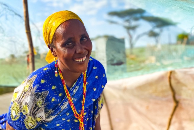 A smiling woman waters the crops she is growing in her kitchen in Kenya
